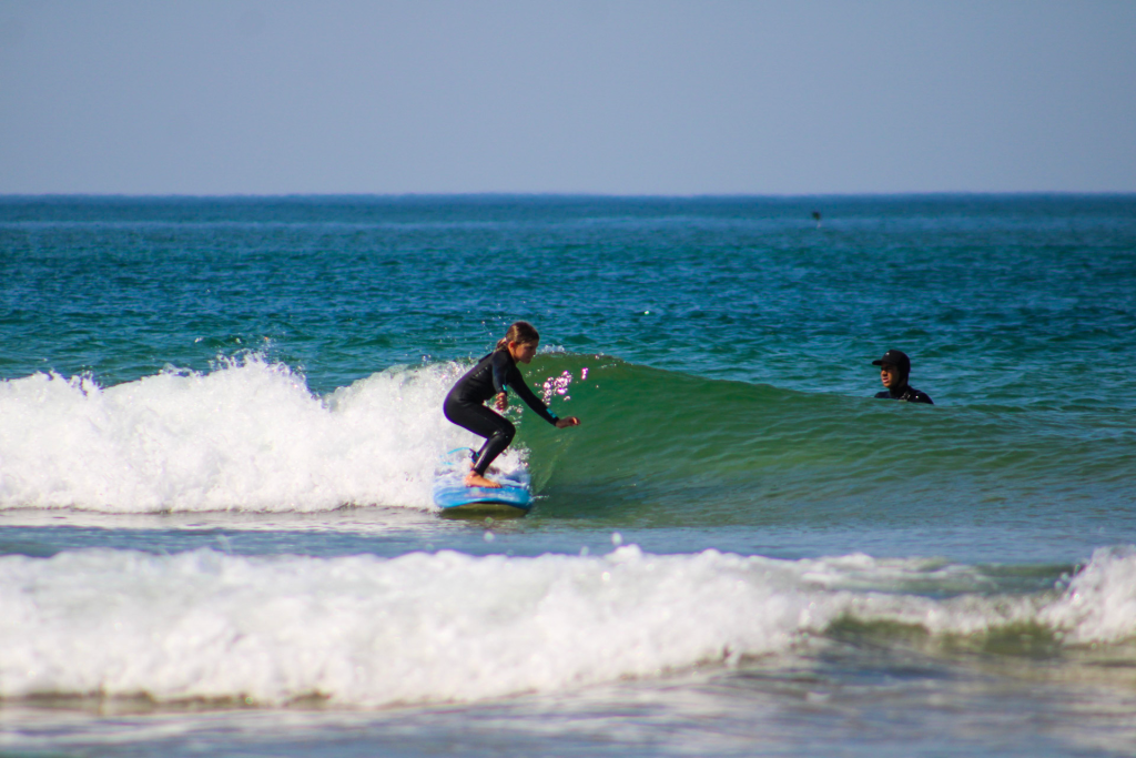Criança em prancha de surf azul a apanhar uma onda em Cascais, com instrutor a observar