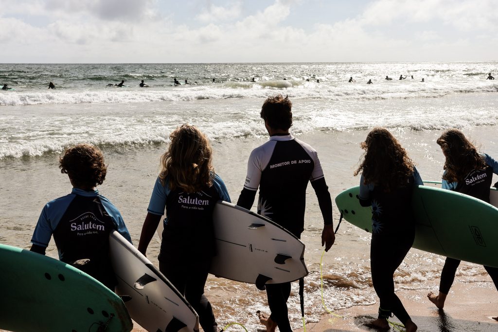 Grupo de alunos e monitor de apoio da Green Wave a caminhar para o mar com pranchas de surf em Cascais