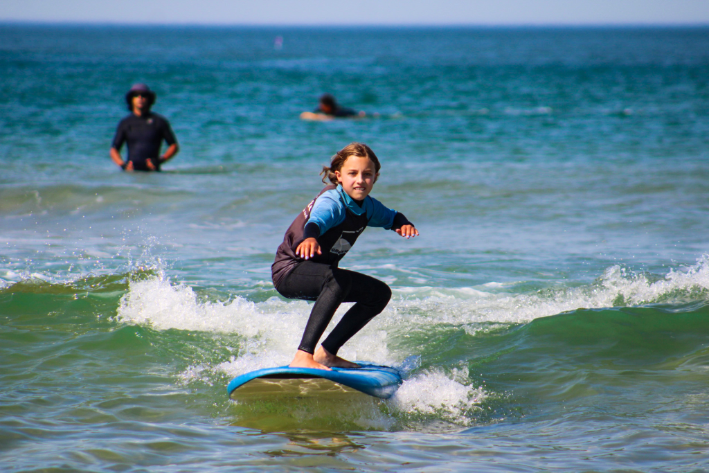 Criança em equilíbrio numa onda durante aula de surf com fato da Green Wave em Cascais
